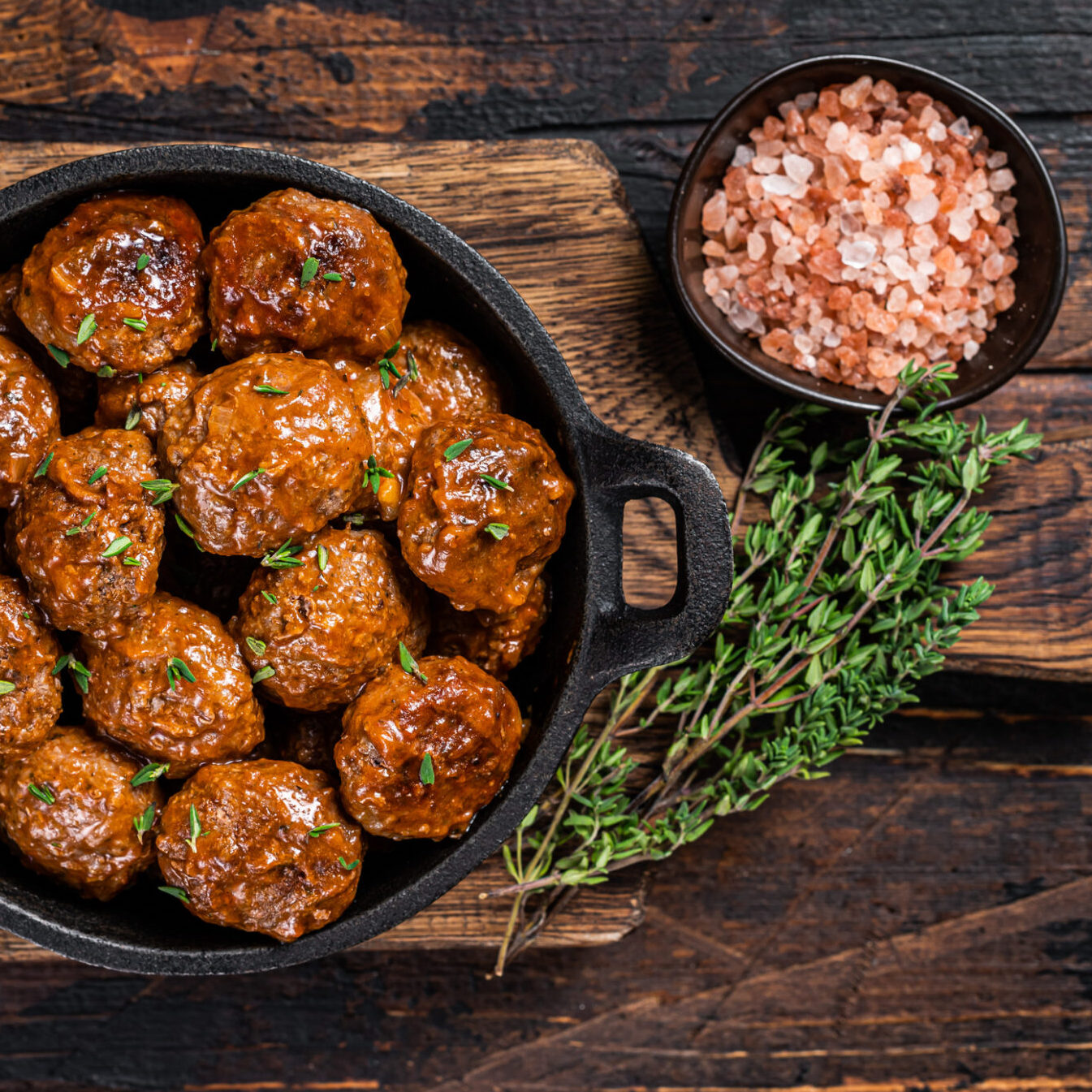 Meatballs in tomato sauce from beef and pork meat with thyme in rustic pan. Dark background. Top view.